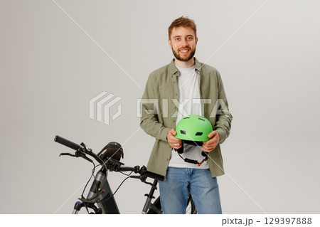 Young man holds green helmet next to electric bike in indoor setting during daytime Young man holds green helmet next to electric bike in indoor setting during daytime 129397888