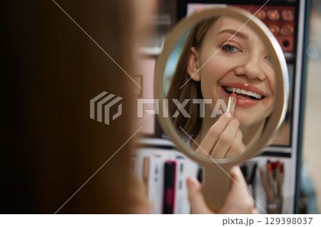A woman is carefully applying bright lipstick while looking in a mirror A woman is carefully applying bright lipstick while looking in a mirror 129398037