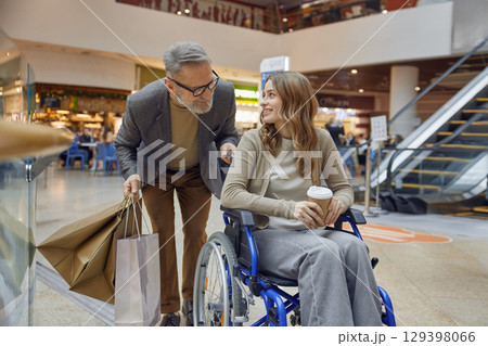 Elderly man assists a woman in a wheelchair in a shopping centre 129398066
