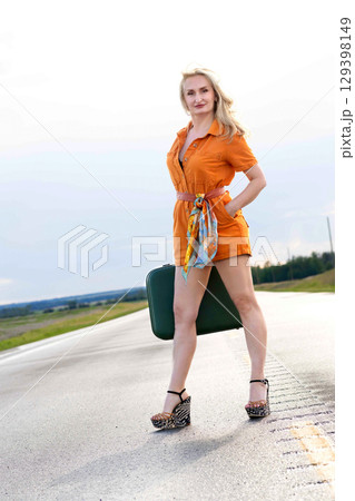 Blonde woman with a green retro suitcase standing on the highway. 129398149