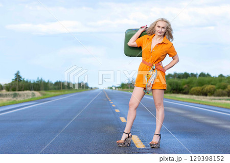 Blonde woman with a green retro suitcase standing on the highway. 129398152