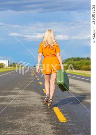 Blonde woman with a green retro suitcase walking on the highway. Blonde woman with a green retro suitcase walking on the highway. 129398153