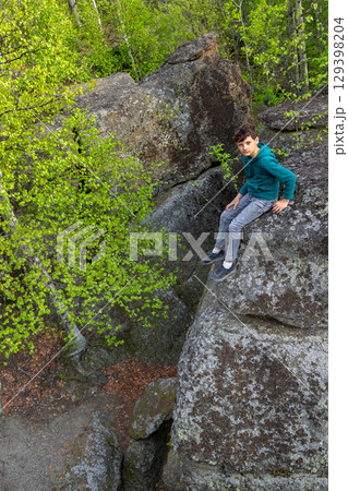 Boy is sitting on big Rocks formation in the green forest. Boy is sitting on big Rocks formation in the green forest. 129398204