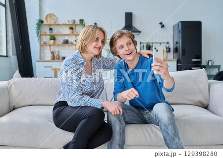 Middle aged mother and teenage son sitting together at home taking selfie photo on smartphone Middle aged mother and teenage son sitting together at home taking selfie photo on smartphone 129398280