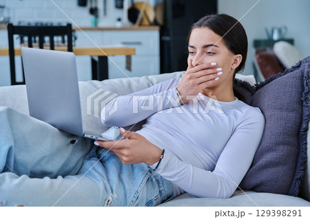 Serious sad stressed teenage girl looking at laptop, lying on sofa at home Serious sad stressed teenage girl looking at laptop, lying on sofa at home 129398291