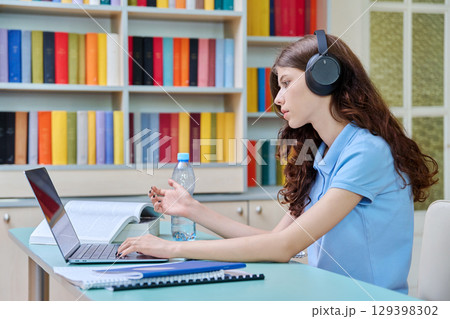 Teenage girl high school student in headphones having video lesson, at library 129398302