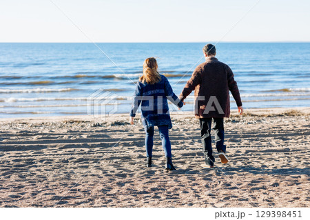 Loving couple walks on beach along sea on sunny autumn day. Weekend and lifestyle concept. Back view. High quality photo Loving couple walks on beach along sea on sunny autumn day. Weekend and lifestyle concept. Back view. High quality photo 129398451