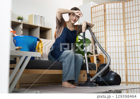 Home Cleaning. Tired woman resting while vacuuming, showcasing the effort of household chores. Home Cleaning. Tired woman resting while vacuuming, showcasing the effort of household chores. 129398464