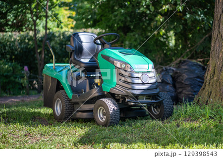 Modern lawn mower, petrol, gasoline powered garden tractor with seat, steering wheel to trim grass 129398543