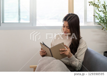 Reading and Relaxation. Young woman reading a notebook in a cozy living room. 129398595