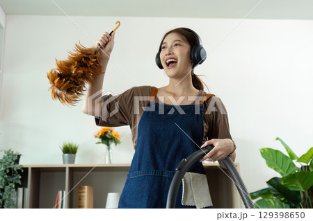 Home Cleaning. Happy woman singing while vacuuming, enjoying music during chores. 129398650