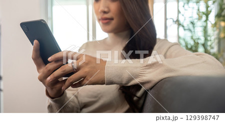 Young woman focused on smartphone while relaxing on couch 129398747