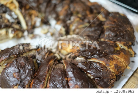 A rustic and appetizing close-up of a freshly baked chocolate babka, or a similar braided cake, with rich dark chocolate filling visible in the layers. 129398962