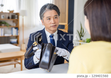 出張買取　査定　訪問先で鑑定をしている男性 129401560