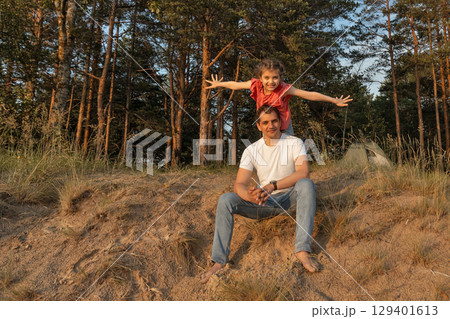 Happy little cheerful daughter on daddy's back with arms to sides playing happy in airplane on sunny beach in summer, lifestyle, , Father's Day Happy little cheerful daughter on daddy's back with arms to sides playing happy in airplane on sunny beach in summer, lifestyle, , Father's Day 129401613