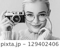 Portrait of a Smiling Woman Holding a Vintage Camera with Stylish Glasses and Cozy Sweater 129402406
