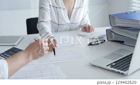 Professional accountant pointing into paper with a pen collaborating, reviewing financial reports with a colleague while using calculator, laptop. Audit and taxes concept Professional accountant pointing into paper with a pen collaborating, reviewing financial reports with a colleague while using calculator, laptop. Audit and taxes concept 129402620