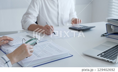 Team of accountants are working together, using a magnifying glass and a calculator, to audit financial reports in office. Audit and taxes in business 129402692
