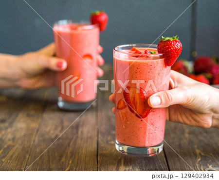 AI generated refreshing strawberry smoothie in a glass held by hand with fresh strawberry pieces cascading down against a dimly-lit cozy cafe background AI generated refreshing strawberry smoothie in a glass held by hand with fresh strawberry pieces cascading down against a dimly-lit cozy cafe background 129402934