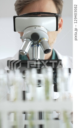 Scientific researcher in protective gear analyzing specimens through a microscope in a sterile laboratory environment. Medicine, healthcare and science concept 129403082