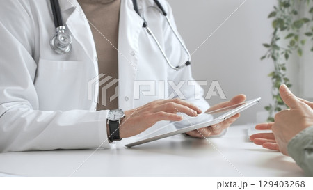 Doctor man in lab coat and stethoscope listening to patient while using tablet in modern medical office. Medicine and health care Doctor man in lab coat and stethoscope listening to patient while using tablet in modern medical office. Medicine and health care 129403268