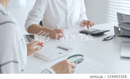 Groupe of accountants collaborating on financial analysis, using a magnifying glass, calculator, and laptop to ensure data accuracy. Audit and taxes 129403308