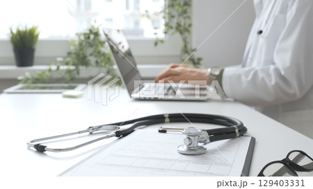 Stethoscope over a medical records are lying on the desk opposite the doctor is typing on a laptop with a in a medical office, suggesting online healthcare or telemedicine services. Medicine concept 129403331