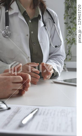 Doctor woman in medical coat is explaining diagnosis to male patient during a medical consultation in a medical office, gesturing with hands, vertical close up view. Medicine and health care 129403720