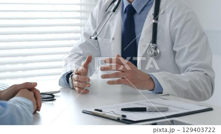 Male doctor explaining diagnosis, gesturing with hand to patient during consultation in clinical setting. Medicine and healthcare concept 129403722