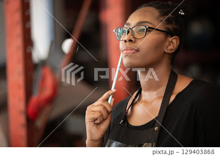 Confident african american female worker holding blue folder while inspecting car parts warehouse. Concept of automotive maintenance, quality control industrial service. Confident african american female worker holding blue folder while inspecting car parts warehouse. Concept of automotive maintenance, quality control industrial service. 129403868