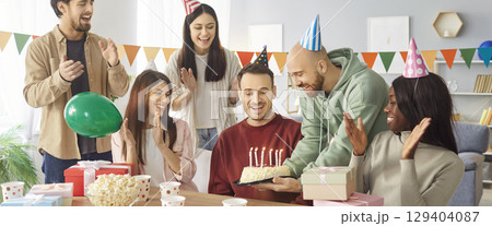 Happy people congratulating a young friend sitting at festive table on birthday party at home. 129404087