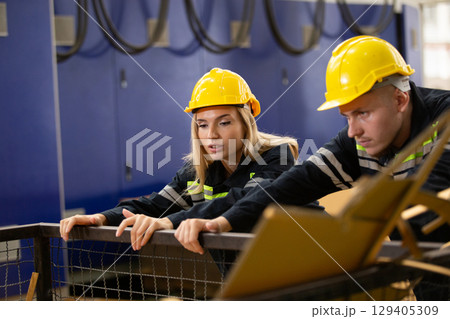 Male and female factory workers wearing safety gear checking cardboard waste in industrial bin. Team analyzing recycling process or material inspection in manufacturing site. 129405309