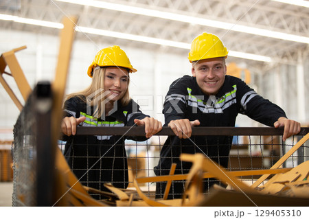 Male and female factory workers wearing safety gear checking cardboard waste in industrial bin. Team analyzing recycling process or material inspection in manufacturing site. 129405310