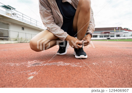 Athletic preparation runner tying shoelaces on track outdoor stadium action shot dynamic environment close-up perspective 129406907
