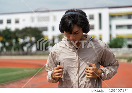 Young Adult Engaged in Outdoor Fitness Routine with Headphones on a Track Field 129407174
