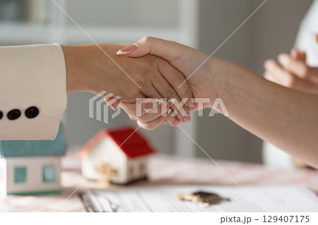 Real Estate Agent Shaking Hands with Client Over Contract and Model House on Table 129407175