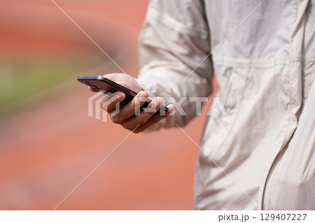 Morning Jogger Holding Smartphone in Park Promoting Fitness and Wellness Lifestyle 129407227