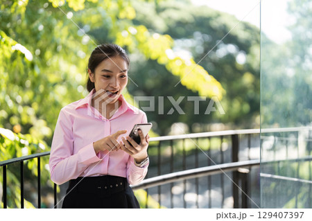 Young Professional Woman Engaging with Mobile Technology in a Vibrant Outdoor Business Environment 129407397