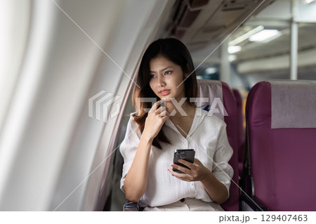 Businesswoman Relaxing on Airplane with Smartphone During Flight, Looking Out Window, Wearing White Blouse, Traveling for Work Businesswoman Relaxing on Airplane with Smartphone During Flight, Looking Out Window, Wearing White Blouse, Traveling for Work 129407463
