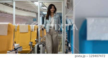 Young Woman Traveling with Luggage in Airplane Cabin, Ready for Adventure and Exploration on a Modern Commercial Flight 129407472