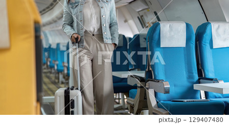 Traveler with Luggage Walking Down Airplane Aisle in Casual Attire, Ready for Journey, Inside Modern Aircraft Cabin with Blue Seats 129407480