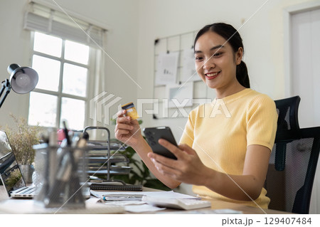 Young Woman Managing Finances at Home with Smartphone and Credit Card for Effective Savings and Budget Planning 129407484