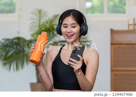 Young Woman Enjoying a Wellness Routine with Music and Hydration in a Modern Home Setting Young Woman Enjoying a Wellness Routine with Music and Hydration in a Modern Home Setting 129407486