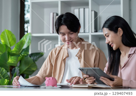 Young Couple Planning Finances Together with Tablet and Piggy Bank for Future Savings and Budgeting in a Modern Home Office Setting 129407493