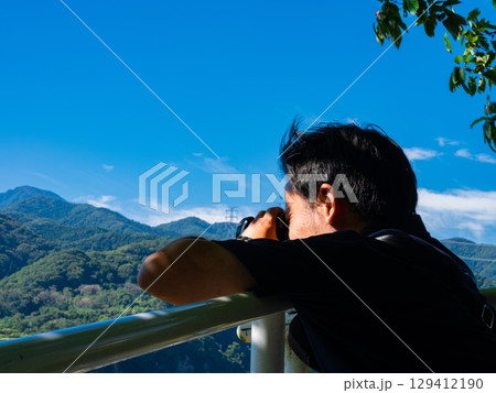 山をバックに写真を撮る男性 129412190