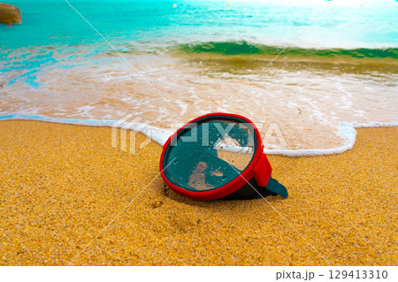 A diving mask lies on a sandy beach and is washed by waves of water 129413310