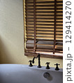 bright bathroom scene featuring white bathtub, wooden blinds, and textured yellow wall. sunlight filters through slats, creating warm and inviting atmosphere 129414270