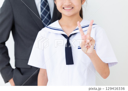 2本指を立てる夏の学生服を着た中学生の女の子とスーツ姿のお父さん 129416336