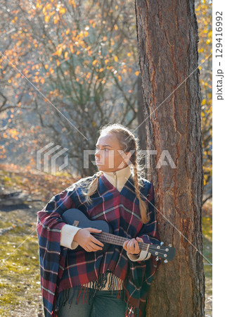 Blonde woman playing guitar ukulele outdoors in autumn forest. Concept of sound therapy, mental health and wellness rituals. Calmness tranquility audio-sensory practices. Aura farming Blonde woman playing guitar ukulele outdoors in autumn forest. Concept of sound therapy, mental health and wellness rituals. Calmness tranquility audio-sensory practices. Aura farming 129416992