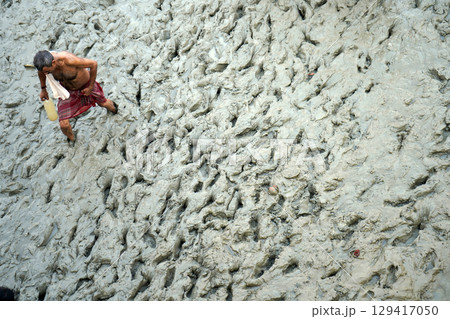 14th October 2023, Babughat, Kolkata, West Bengal, India. Man Walking Through Muddy Terrain with a Bottle 129417050